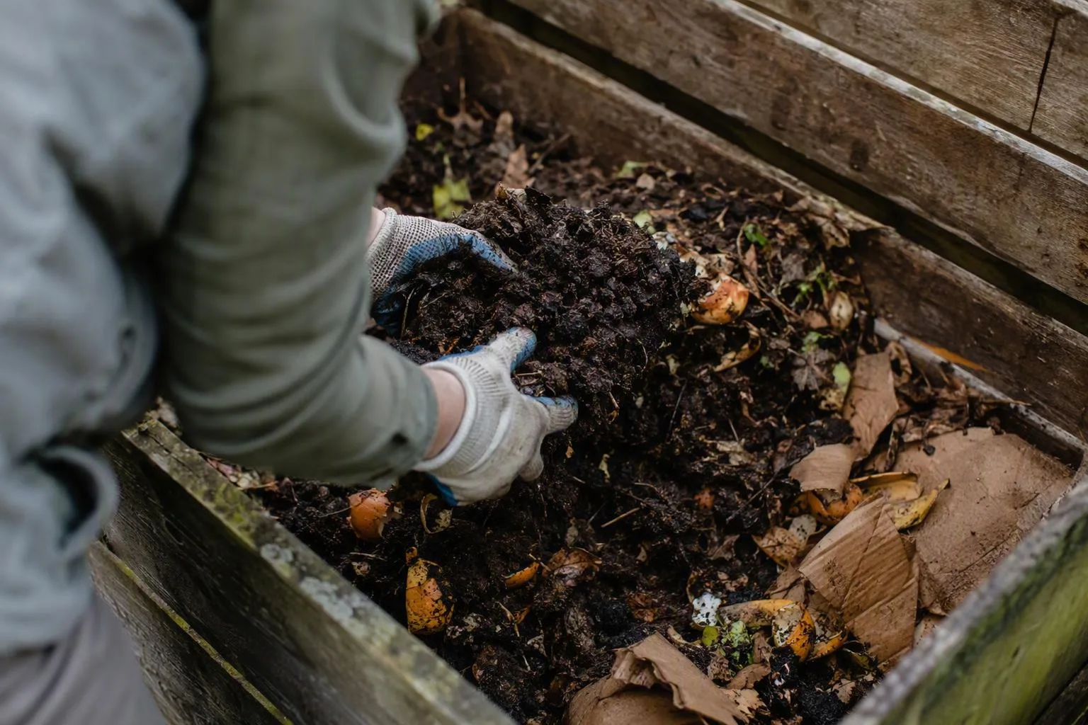 Gloved hands mix a dense compost center with dry leaves to improve airflow in the heap.