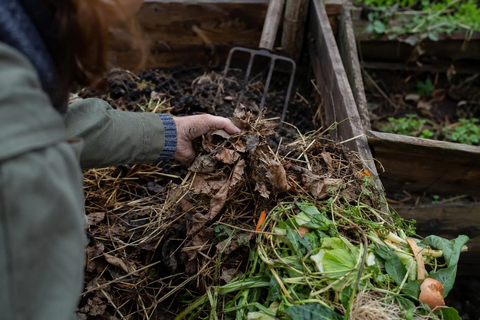 A gardener separates dry leaves from moist vegetable scraps beside a compost pile to show how each material contributes.
